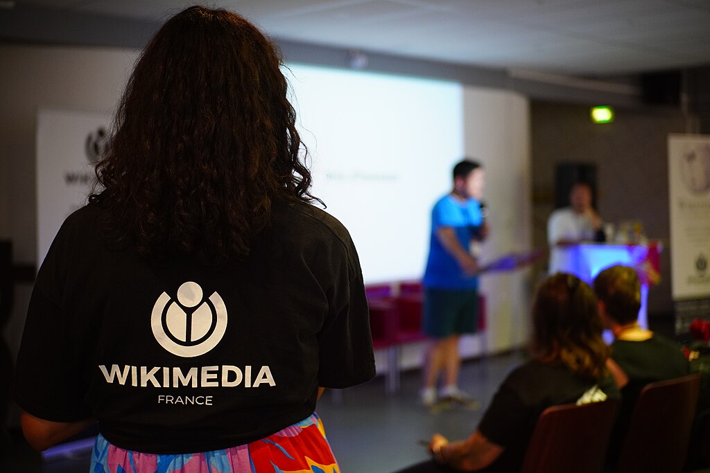 Un atelier de Wikmédia France, au premier plan une femme de dos porte le T-shirt de l'association.