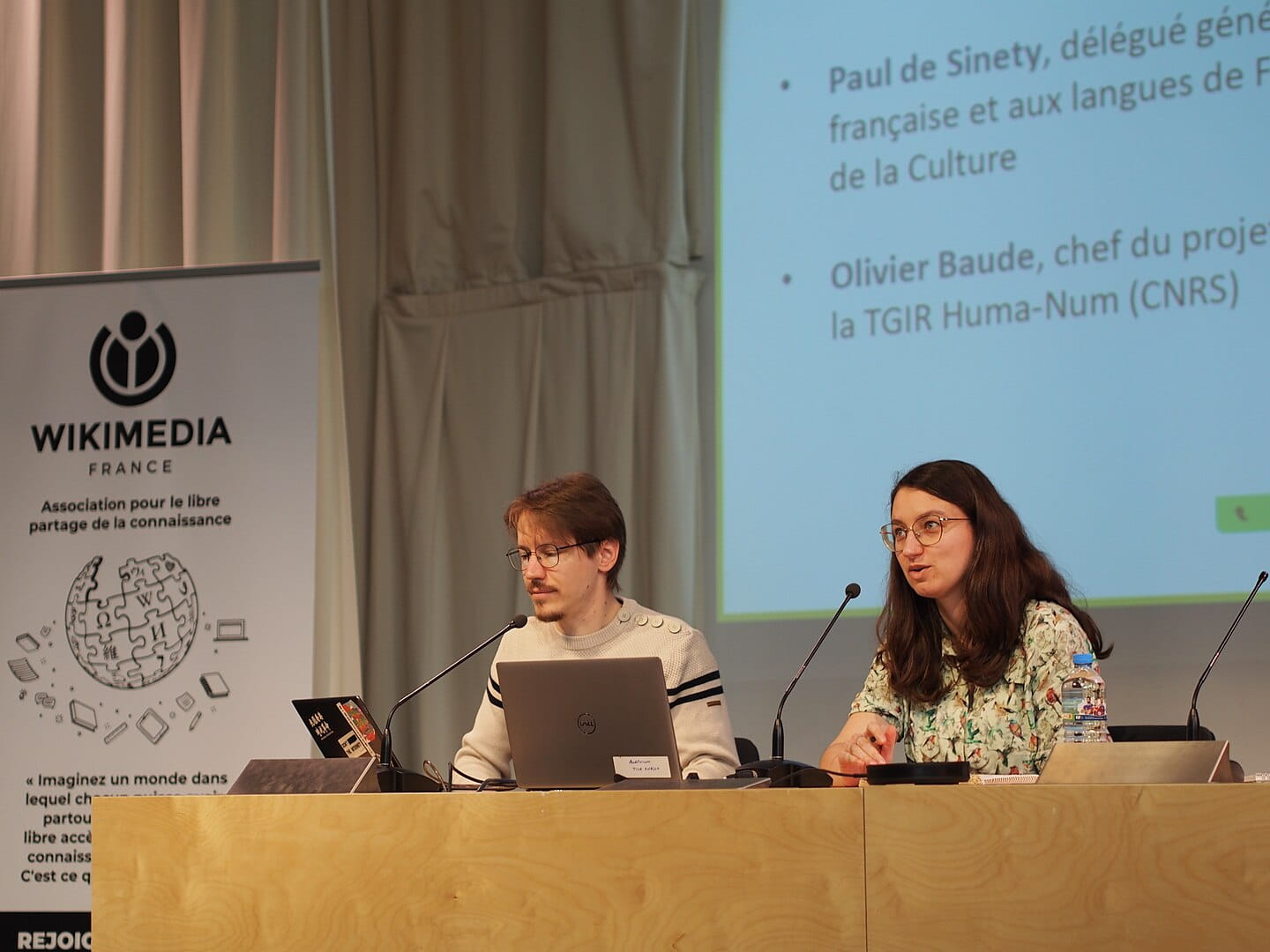 Un homme et une femme devant des micros lors d'une conférence Wikimédia France
