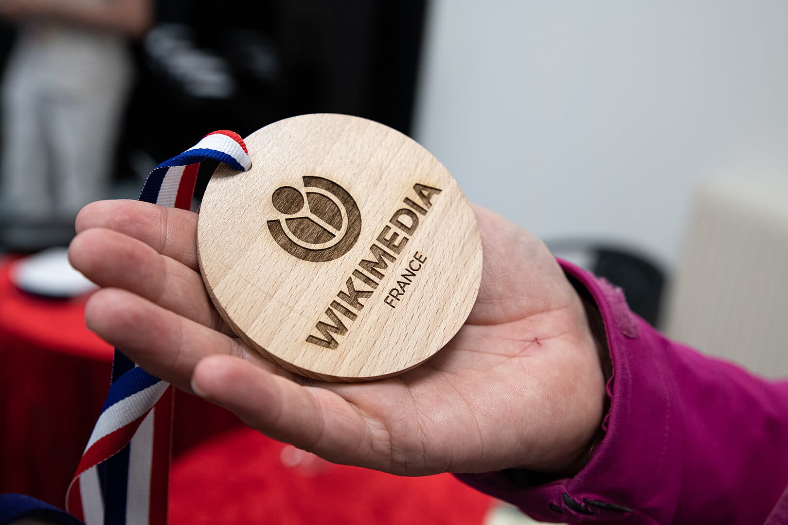 Une médaille en bois de Wikimedia France dans une main ouverte